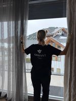 Hausreinigungskraft öffnet Vorhang mit Bergblick